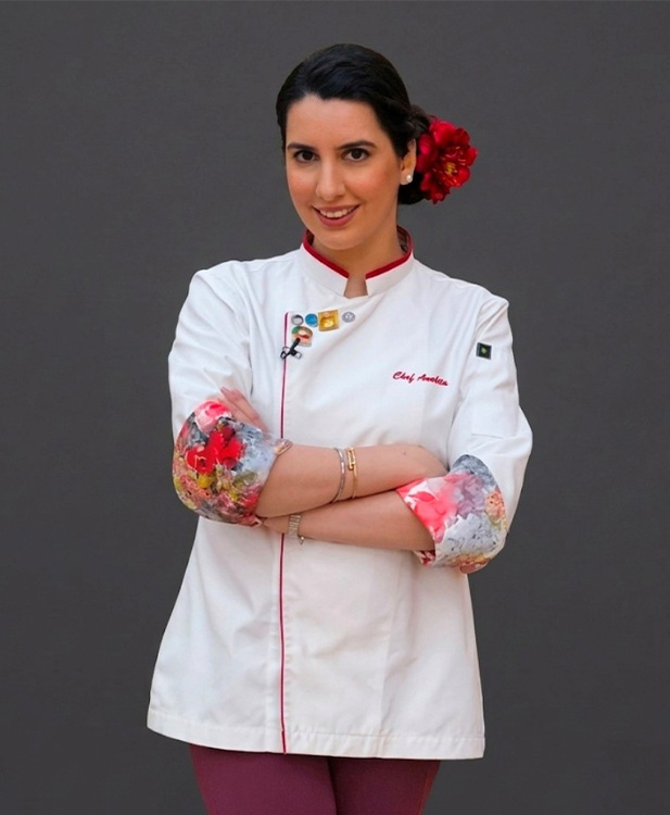 female chef wearing a white coat with floral sleeves smiling confidently posing with arms crossed showcasing culinary skills and expertise in five star cuisine
