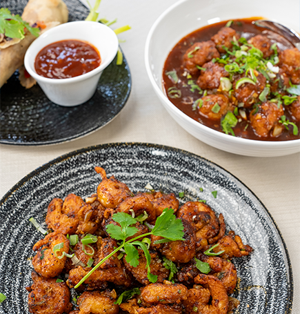 Three plates of vibrant Asian cuisine featuring crispy battered shrimp garnished with herbs and chili sauce alongside flavorful chicken in a sweet and spicy sauce.