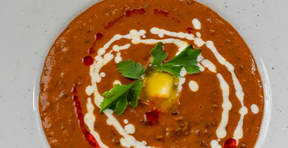 bowl of rich and creamy lentil soup topped with fresh cilantro and a swirl of cream showcasing three delicious garnishes