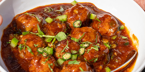 bowl of meatballs in spicy sauce garnished with green onions and cilantro showcasing a delicious dish with three meatballs visible