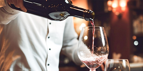 person pouring red wine into a glass in an elegant setting showcasing wine serving techniques